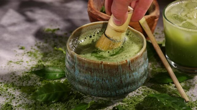 Hand whisking vibrant green matcha tea with traditional bamboo whisk, surrounded by matcha powder and tea-making ingredients. Illuminated by natural sunlight, creating an authentic tea ceremony scene