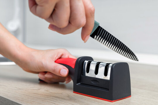 A housewife sharpens a kitchen knife, close-up. knife sharpening process. sharpening a kitchen knife in the home kitchen. manual sharpener for a kitchen knife