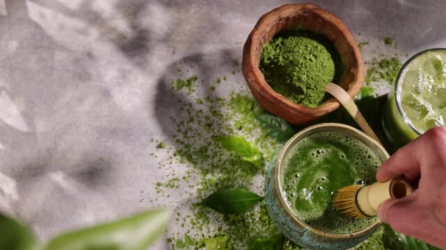 Hand whisking vibrant green matcha tea with traditional bamboo whisk, surrounded by matcha powder and tea-making ingredients. Illuminated by natural sunlight, creating an authentic tea ceremony scene