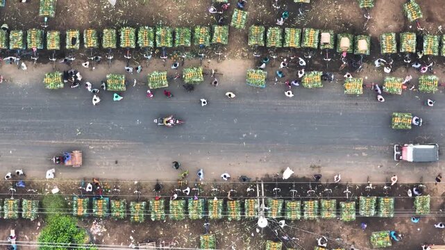 Aerial view of a bustling local fruit market with rows of carts and people along a roadside in Madhupur, Dhaka Division, Bangladesh.