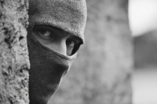 Mann in Kapuzenpullover schaut mit intensivem Blick hinter einer Mauer und beobachtet eine Situation, Symbolbild f&uuml;r Einbrecher, Gangster, Krimineller, Kriminalit&auml;t, Verbrecher, Dieb, bedrohliche und be&auml;ngstigende Stimmung, AI generiert, AI generated