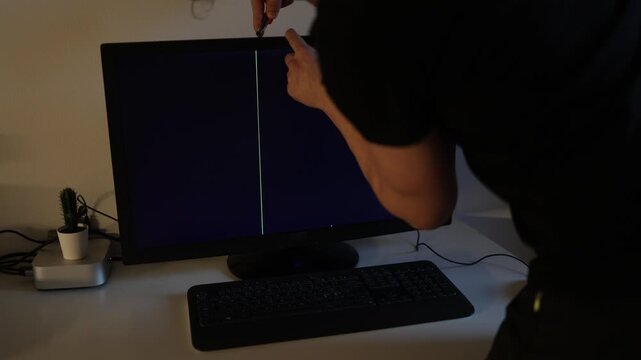 Young man tries to repair a computer monitor with a black screen and a vertical line in the middle highlighting hardware failure troubleshooting and technical support concepts