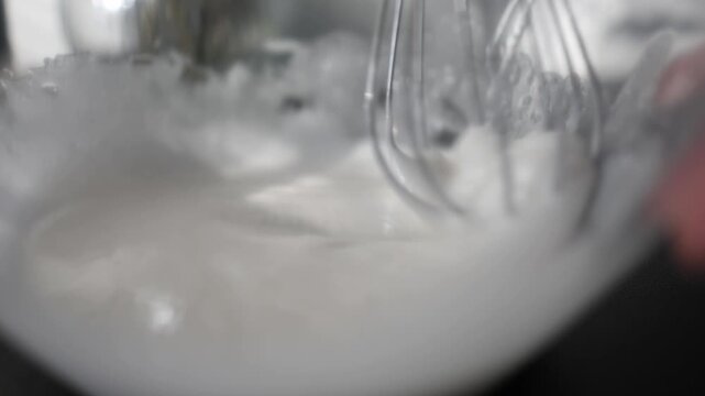 Close up view through a transparent glass bowl as a whisk beats egg whites into a light foam Smooth kitchen process with focus on texture movement and baking preparation