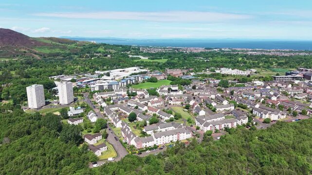 Aerial panoramic view over Greendykes and Niddrie residential suburban areas in Edinburgh, Scotland. Scenic flight above modern houses, neighborhood streets, and green trees with the Firth of Forth es