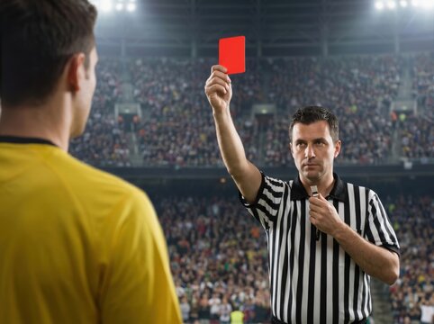 Professional soccer referee holding a red card during a tense match in a crowded stadium with football