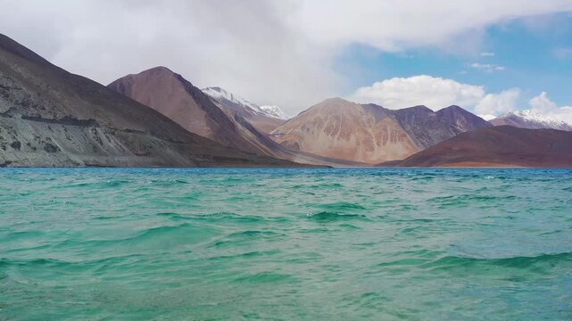 Cinematic low flight over blue water rising to snowy peaks at Pangong Lake Himalayan mountains. . High Altitude Lake in Greater Himalayas