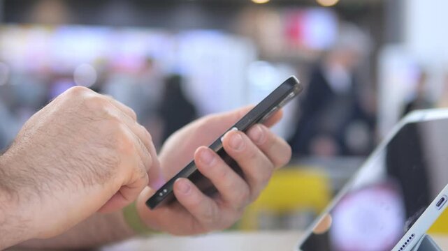 Hands tap smartphone screen, fingers move fast and precise. Background blurred with bright lights and tech equipment. Person focused, engaged, multitasking with digital device