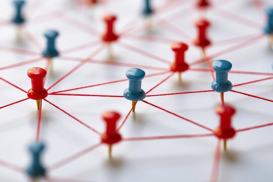 Network of red and blue push pins connected by string on a white surface in an office setting during the day