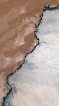 Seamless rotating vertical aerial view of desert and rocky terrain boundary with geological patterns satellite view from space