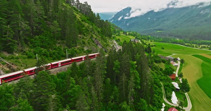 Aerial video of the red train traversing the Landwasser viaduct. The Swiss Express travels through the green meadows and mountains of Switzerland. Passenger transportation in Switzerland