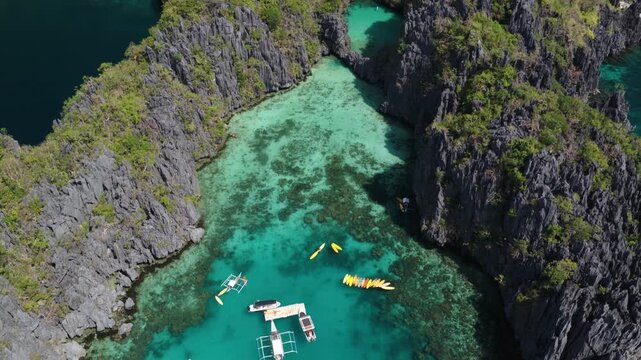 Aerial view of traditional bangka boats and yellow kayaks floating on the turquoise waters of Big Lagoon surrounded by limestone cliffs in El Nido, Mimaropa, Philippines.