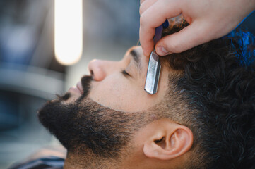 Fototapeta premium Barber shaving man's beard hairline with straight razor