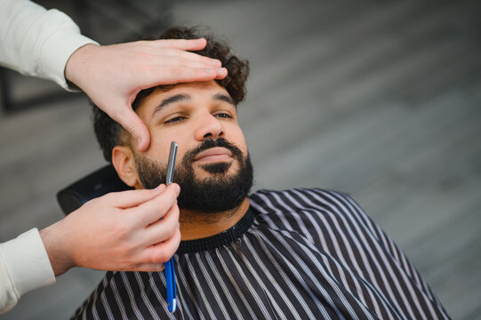 Barber giving man beard trim with straight razor