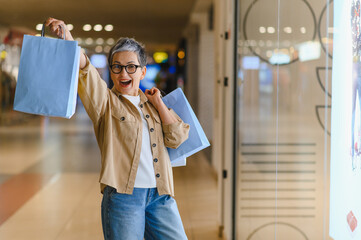 Fototapeta premium Happy mature woman celebrating successful shopping in mall