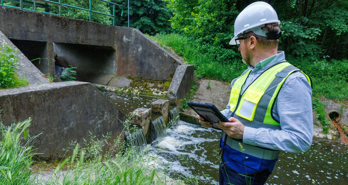 Ecologist hydrologist working near river weir for flood prevention and environmental protection. Environmental engineer inspecting a dam and water level control system for ecological monitoring. 