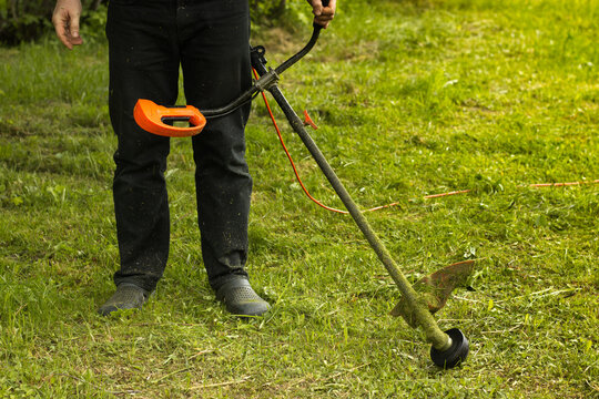 Man holding a string trimmer and cutting grass in a garden