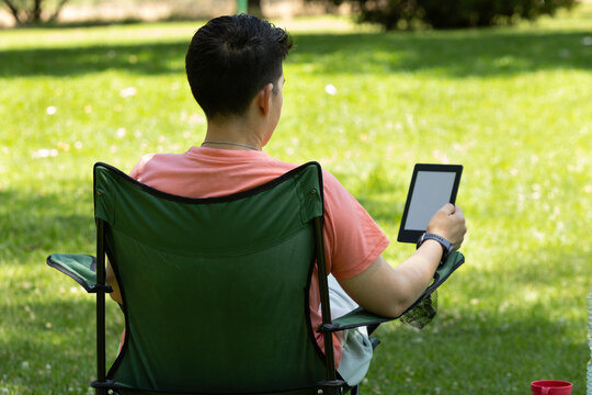 Young caucasian man reading ebook outdoors in green park