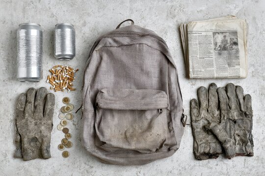 A collection of discarded items including a backpack, dirty gloves, cigarette butts, coins, and newspapers.