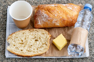 Naklejka premium A rustic picnic spread featuring a crusty loaf of bread, a slice of butter, and a bottle of water.