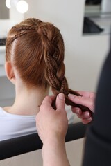 Fototapeta premium Hairstylist braiding teenage girl's hair in salon, closeup