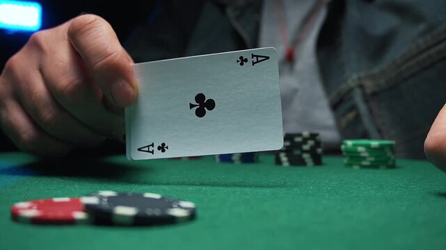 Player reveals ace of clubs while placing poker chips on green felt table, showcasing strategic decision-making in a card game setting