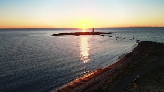 Aerial view of Grotta Lighthouse standing on a small island at sunset with golden light reflecting on the ocean and a coastal path Seltjarnarnes, Seltjarnarnesbaer, Iceland.