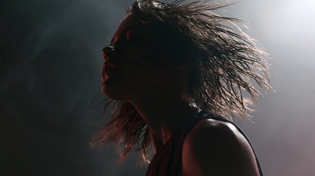 Medium shot of a nonbinary dancers wet hair flowing through the frame in slow motion accentuated by dramatic rim lighting against a dark misty studio backdrop