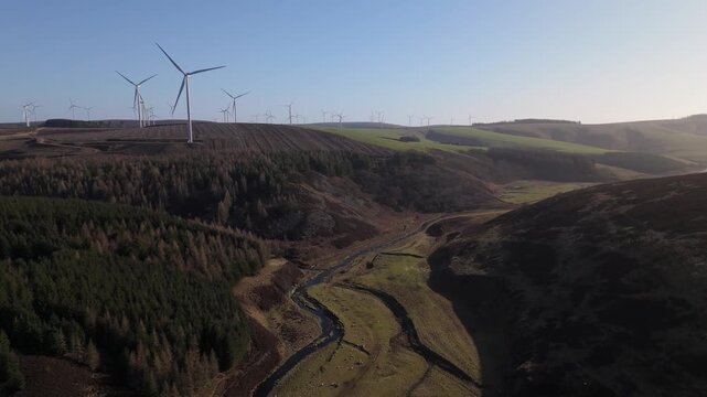 Aerial view of Crystal Rig Wind Farm with wind turbines on rolling hills and a valley stream under a clear sky in Dunbar, Scotland, United Kingdom.