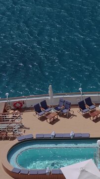 High angle view of a luxury cruise ship deck with a turquoise swimming pool hot tub and sun lounger chairs by the blue ocean
