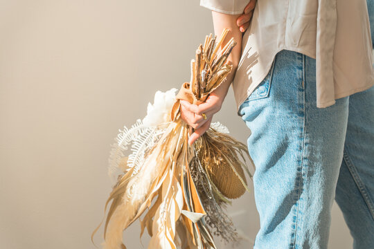 A woman holding a swag of dried flowers by a window bathed in the setting sun (model, fashion, light, shadow)