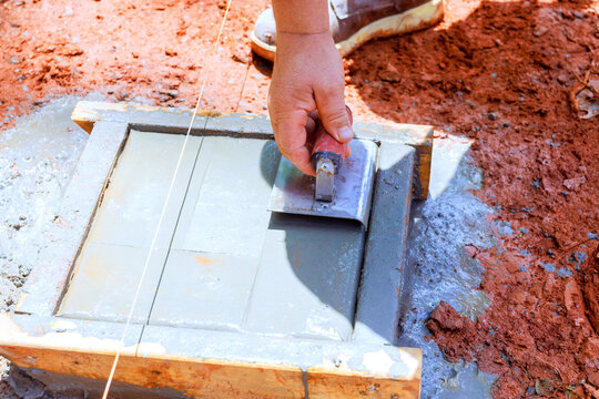 Worker uses trowel to spread edge concrete into wooden mold on construction site