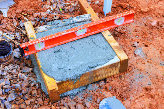 Workers pour concrete into wooden frame while using level tool to check surface
