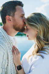 Fototapeta premium Couple shares a moment by the water during a sunny day in a park while displaying affection towards each other