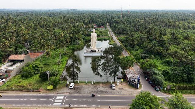 Aerial view of the Tsunami Honganji Viharaya Buddha statue surrounded by a pond and lush palm trees in Peraliya, Southern Province, Sri Lanka.