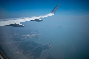 Fototapeta premium Airplane wing flying over the blue ocean coastline with islands.