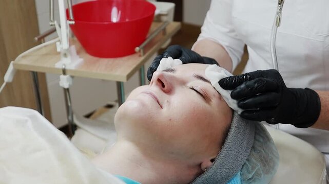 A female doctor, a professional cosmetologist, prepares a patient's face for a procedure