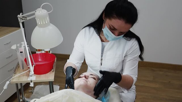 A female doctor, a professional cosmetologist, prepares a patient's face for a procedure