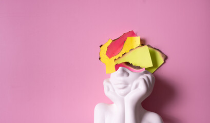 Burnout concepts represented by a bust sculpture and colorful paper pieces on a pink background © Alina