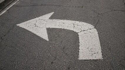 Fototapeta premium White painted left turn arrow on cracked asphalt road surface.