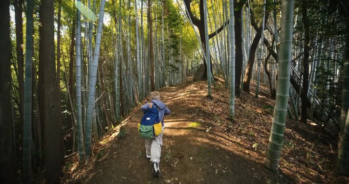 Young child with backpack running on dirt path through bamboo grove in Japan - slow motion steady cam