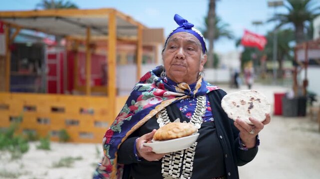 Elderly mapuche woman in traditional attire proudly displaying local chilean food like empanadas