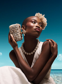 Editorial fashion portrait of gorgeous photo model wearing avant garde white haute couture dress with luxury pearl necklace and shell clutch on wooden pier at tropical turquoise summer beach