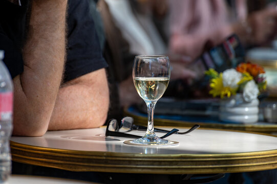 Glass of white wine on outdoor cafe table in heart of Montmartre, leisurely Parisian lunch for locals and visitors, timeless European caf&eacute; culture in Parisian neighborhood