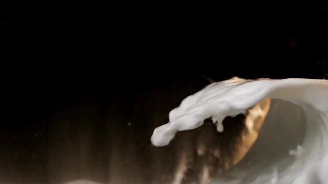 Dynamic closeup of a creamy white liquid wave with golden undertones splashing against a dark background creating an elegant and fluid motion
