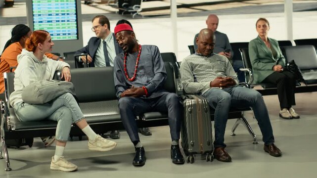 Multiethnic people in crowded bus station hub ready for intercity travel. African American traveler in traditional clothes becoming friends with a woman while waiting on express long-haul coach.