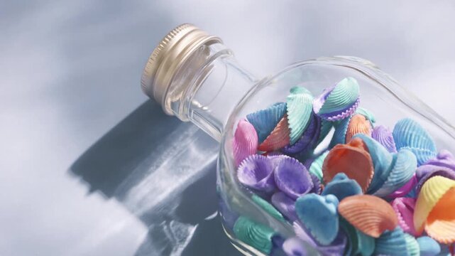 Colorful seashells in a glass bottle with ocean wave shadows and tropical summer concept
