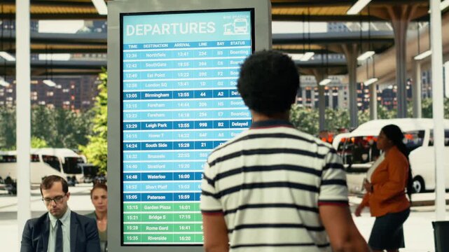 Black commuter gathers near information board in busy city bus station during rush hour, waiting for urban transport commercial services. People in a fast-paced public transportation hub.