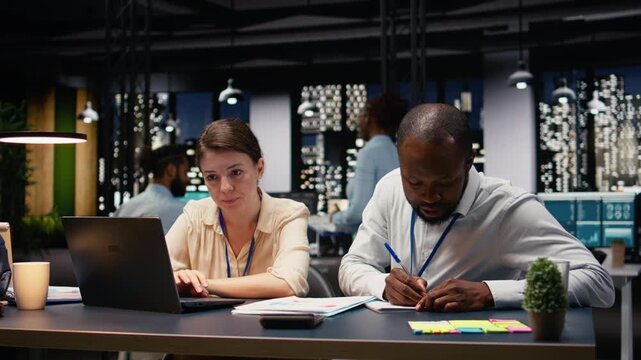 Diverse business team working together in office late at night, collaborating on project development and task management. Coworkers review data and document insights, effective teamwork.