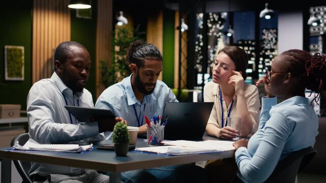 Staff members in modern inclusive office reviewing progress on project. Coworkers presenting team leader key data statistics after business audit, working late at night for development.