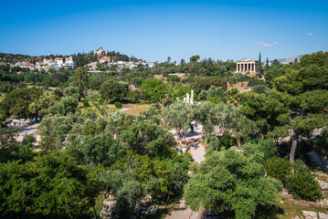 Obraz premium The Ancient Agora of Athens with a clear sightline toward the Temple of Hephaestus and Lofos Nymphon hill in the distance, set beneath a bright blue sky.